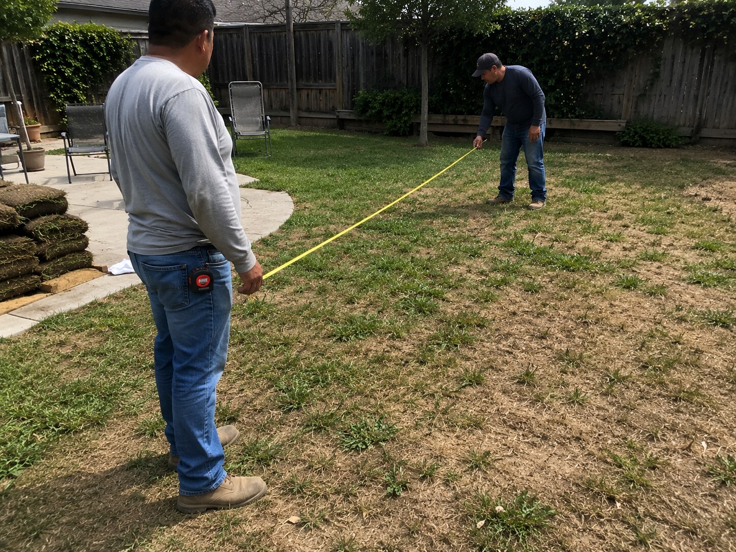 People measuring a backyard lawn before a sod installation